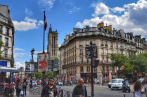 "centro parigi con palazzi antici persone auto e semaforo in primo piano"