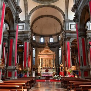"interno chiesa con colonne rivestite in rosso cupola e altare al centro"