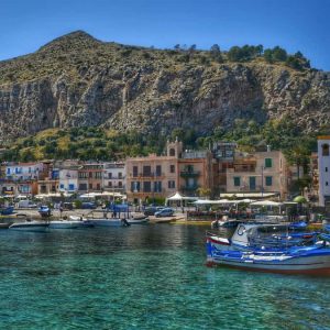 "barche da pesca ormeggiate mare limpido montagna sullo sfondo"