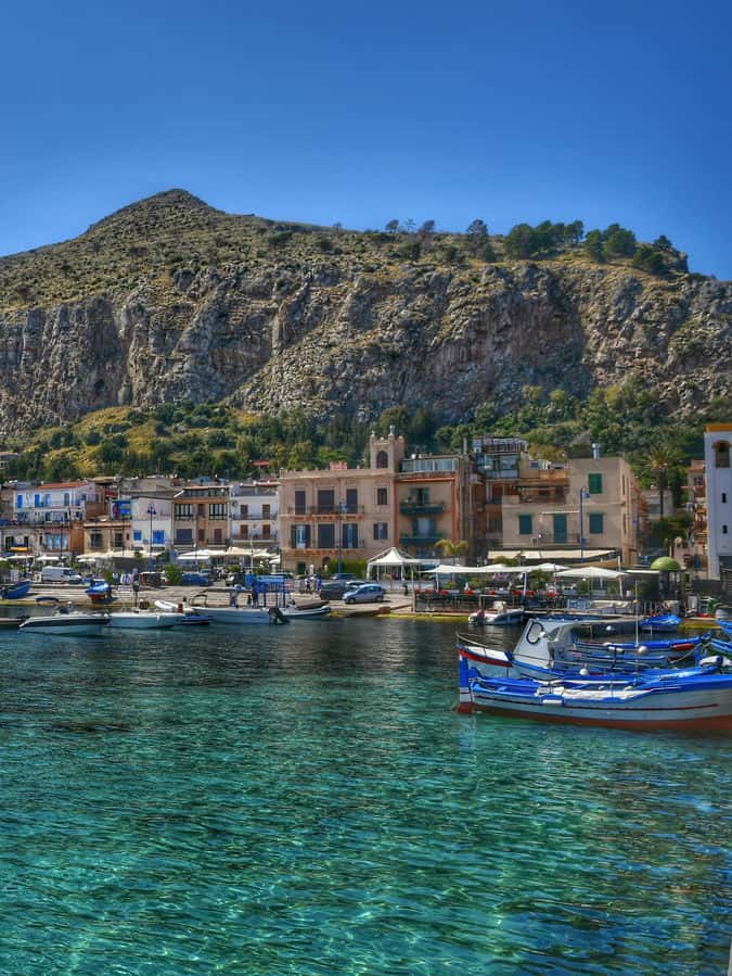 "barche da pesca ormeggiate mare limpido montagna sullo sfondo"