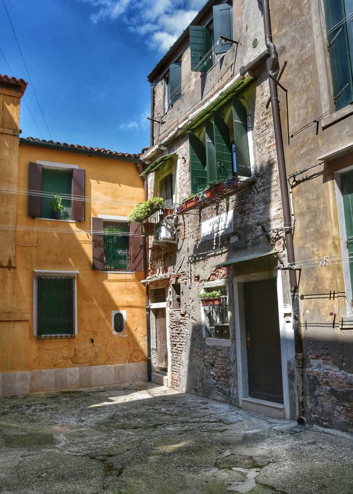 "piccola corte con porta e poggiolo fiorito e casa gialla di fianco"